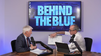 University of Kentucky Executive Vice President Eric Monday presents a diagram on a whiteboard to host Craig Collins during an episode of the "Behind the Blue" podcast.