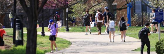 Students walk along a sun-dappled path lined with blooming redbud trees on the University of Kentucky campus during a warm spring day on April 2, 2026.